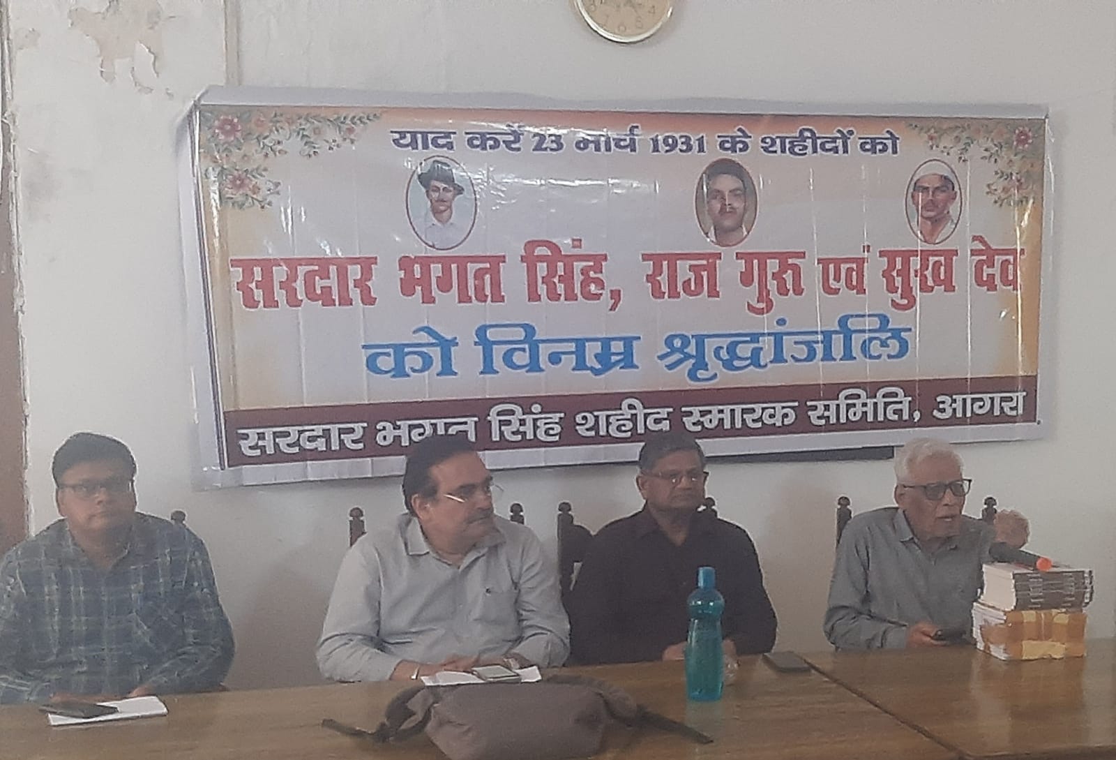 Members of Shaheed Smarak Agra seated at a tribute assembly beneath a banner honouring Bhagat Singh, Rajguru and Sukhdev, observed on Shaheed Diwas, 23 March